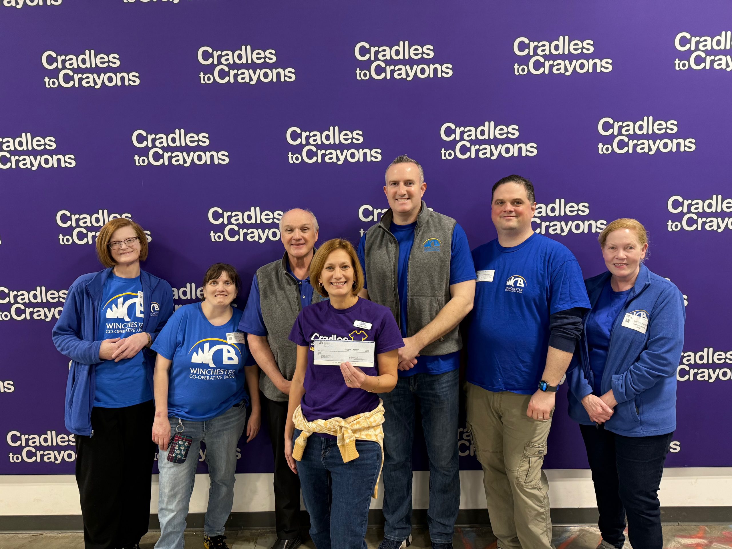 group of employees in front of purple backdrop with crayons
