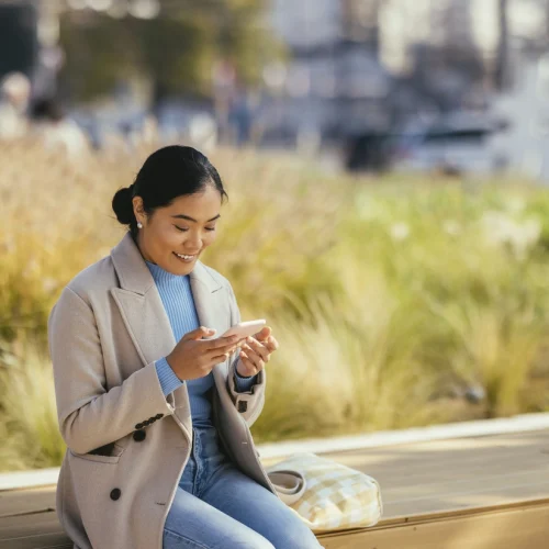 Woman standing outside, looking at her mobile device.